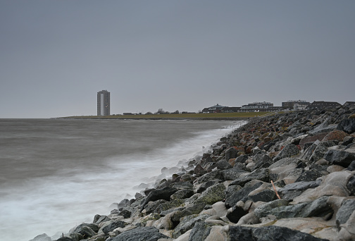 Long exposure: waves and high-rise building on the dike in Büsum at dusk