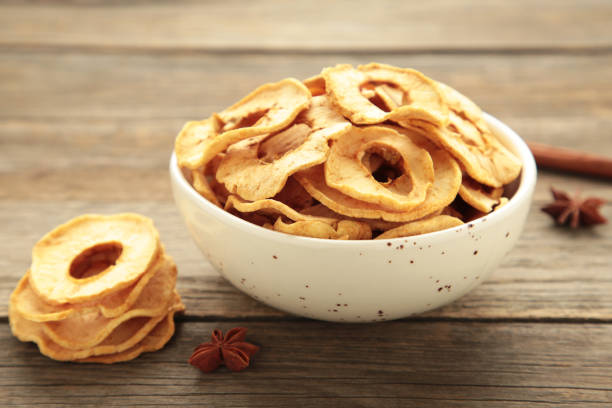 Dried apple chips in a bowl with fresh apple on grey wooden background. Top view