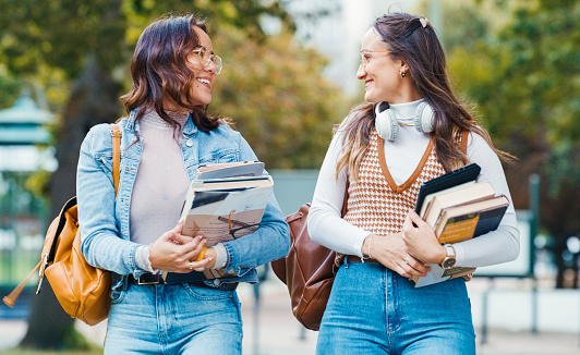 Happy woman, students and walking with books in park for education, literature or outdoor conversation. Female person or academic learners smile with backpack and textbooks for reading or learning