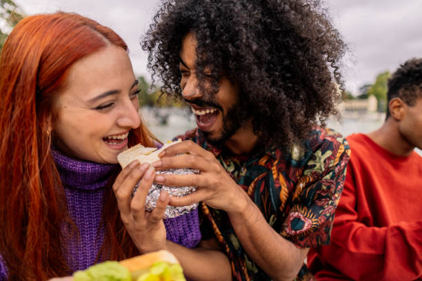 istock ethnic friends sharing a sandwich and laughing 1988240854
