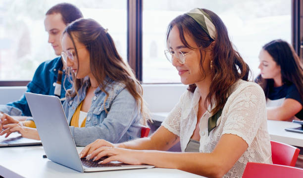istock Woman, students and laptop in classroom for online studying, college research and e learning resources. Happy teenager typing on computer for high school planning, information and scholarship essay 1988242948