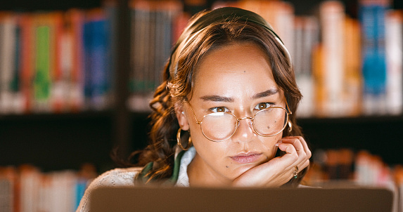 Asian woman, student and laptop with glasses in research or study for education, information or learning. Face of serious female person, learner or scholar reading or thinking on computer by books