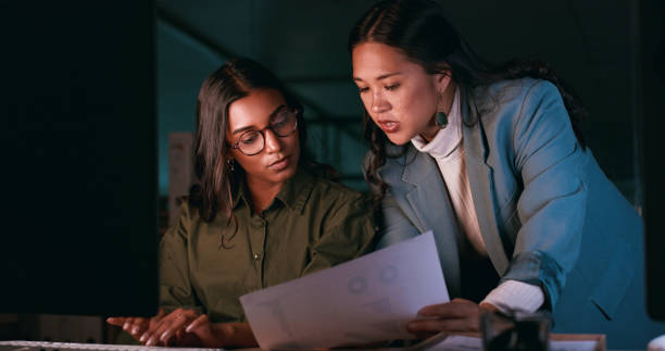 istock Business people, night planning and computer for teamwork, research and data analysis report or documents. Women, leader and analyst with paperwork statistics, deadline help and advice in dark office 1988276579