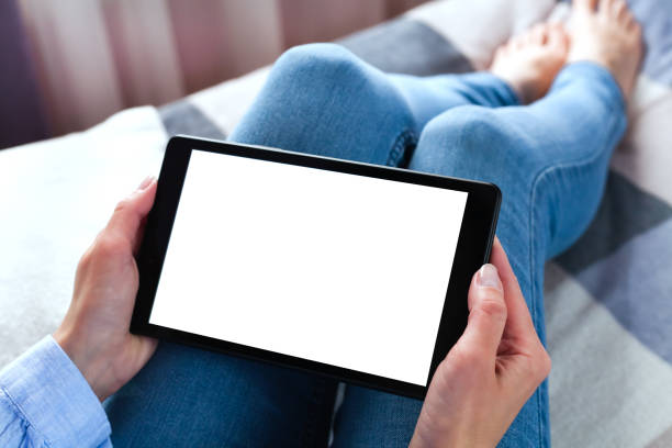 istock Woman holding digital tablet with blank white desktop screen sitting on the bed. Tablet blank screen mockup. Close-up. Copy space. 1988310517