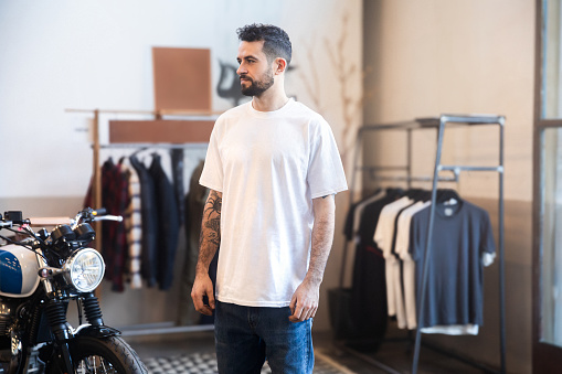 Portrait of tattooed young man in motorcycle garage store wearing white t-shirt\nMockup white t-shirt