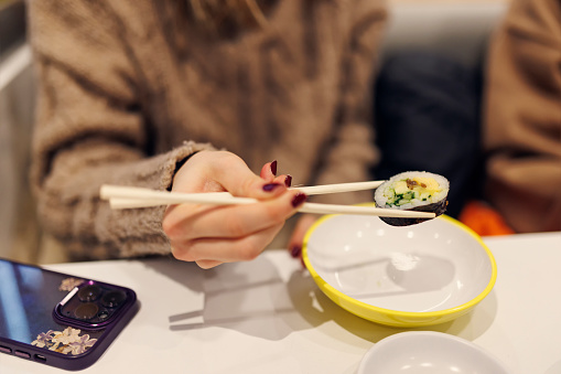 Teenage girl are enjoying Japanese sushi food. The girl is eating a piece of sushi with chopsticks.\nShot with Canon R5