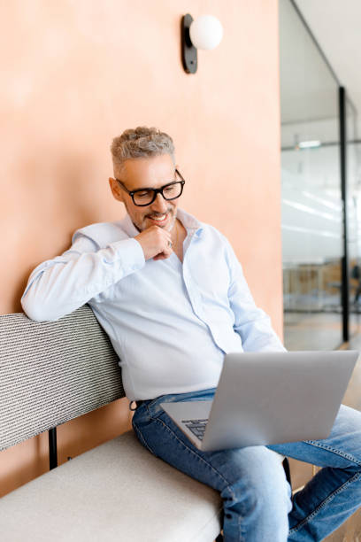 istock Leaning back on a sofa mature businessman appears deeply engrossed in his laptop, indicating intense focus or the discovery of project idea 1988364005