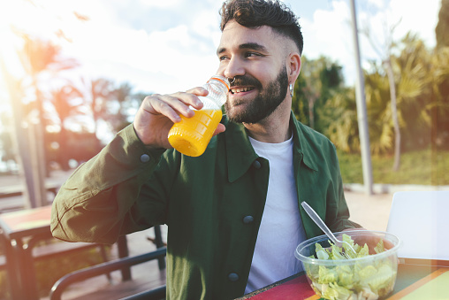 Young man drinking orange juice and eating salad in a park.