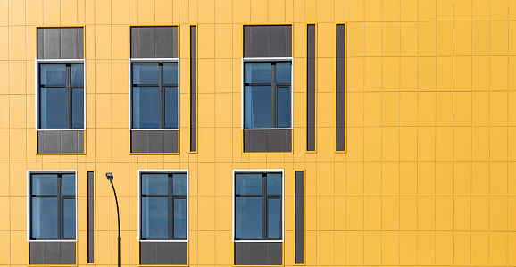 Yellow ventilated facade of a building wall with windows. fragment of an office building. Architectural or building background. Copy space