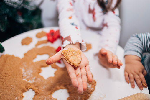 A child is holding a gingerbread and showing it. A little girl makes Christmas cookies, and using a cookie cutter, she is proud of herself and shows off a perfectly cut cookie.