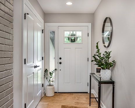 A cozy entryway with brown and brick walls, hardwood flooring, decorations, and a white front door with windows.