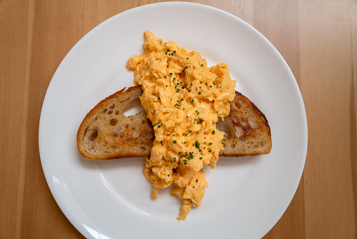 Scrambled egg served across a slice of buttered sourdough toast on a white plate.