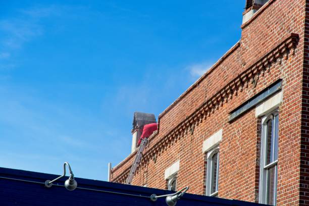 istock Maintenance worker on brick building roof against blue sky 1988494918