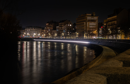 Photo of a car's headlight trails on a cement river bank at night. The river is the Isere, the city is Grenoble, France.