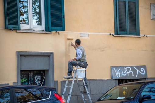 Roma, Latium - Italy - 11-26-2022: A diligent worker paints over graffiti, restoring the clean look of the building's faÃ§ade