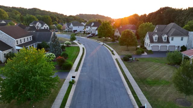 Upscale USA neighborhood during summer sunset. Aerial flight over street with large mansions in suburb.