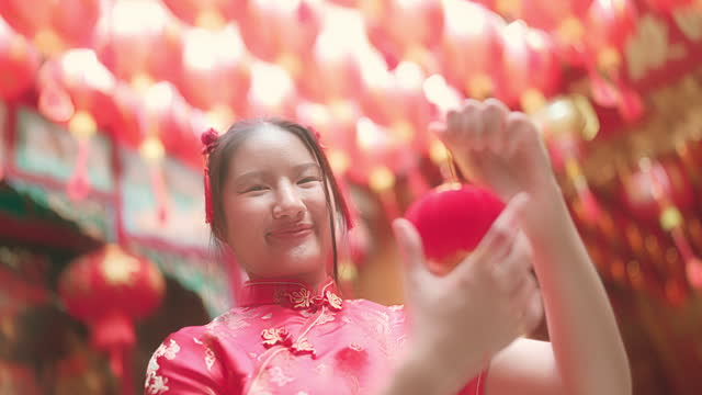 youthful, red-haired Asian girl Cheongsam is playing with a crimson paper lantern.grinning broadly while facing the camera in the Chinese temple.