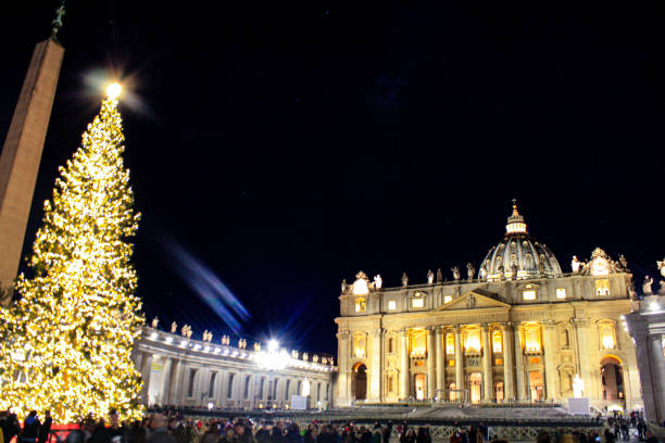 Vatican City (Rome- Italy) - December 2019: Christmas tree at St Peter's Square in front of St Peter's Basilica. Part of the Obelisco Piazza San Pietro Città del Vaticano (the Vatican Obelisk) can be see, though it may be out of focus. The square is moderately busy because of the Christmas festivities.