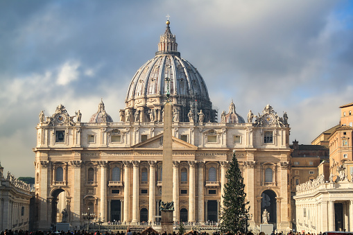 Vatican City (Rome- Italy) - December 2019: Christmas tree at St Peter's Square in front of St Peter's Basilica. Part of the Obelisco Piazza San Pietro Città del Vaticano (the Vatican Obelisk) can be see, though it may be out of focus. The square is moderately busy because of the Christmas festivities.