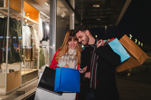 Beautiful young couple holding shopping bags while window shopping in the evening.