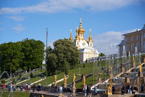 Saint Petersburg, Russia - June 09, 2023: Golden monuments with fountains and Grand Palace in Peterhof park near St. Petersburg with blue sky. Built in 18th century laid out on the orders of Peter the Great. The palace-ensemble with fountains, gardens and monuments is recognized as a UNESCO World Heritage Site.