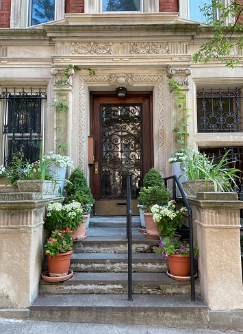 Front stoop of an elegant townhouse on a hill with potted flowers and plants along the steps in the Hamilton Heights neighborhood of Harlem, New York City in the summer