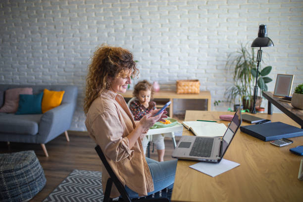 istock Young mother working and using phone while taking care of her baby 1988673748