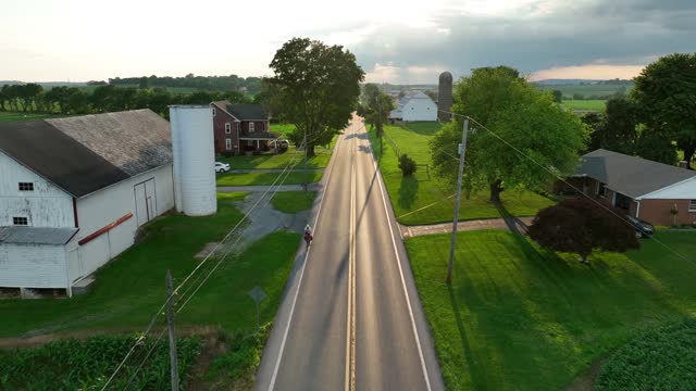 Car driving on a rural road through lush green fields with farmhouses and trees. Aerial during summer in American countryside.