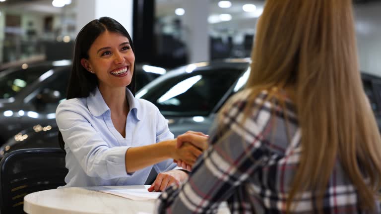 Beautiful saleswoman handing the keys of a new car to unrecognizable customer at a car dealership