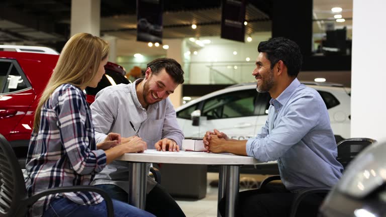 Happy couple signing the paperwork to buy a car at the dealership looking very excited