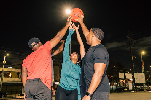A group of five friends holding a basketball in the air while inside a concrete court at night.