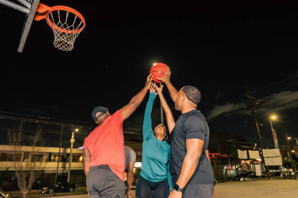 four friends holding basketball to the air at night - city night lighting equipment mid air imagens e fotografias de stock