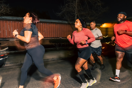 A blurred action shot of a group of friends, two Hispanic people and two Black people, jogging to the left while on a nighttime run in Los Angeles.