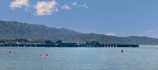 Santa Barbara, CA, USA - January 28, 2024: Stearns Wharf pier with buildings on top. Wide landscape with ocean up front, mountain range, all under blue cloudscape