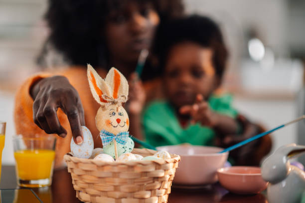 istock Close up of interracial mother putting easter egg into a basket on table. 1988812091
