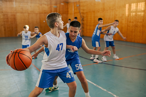 A young basketball players in action are practicing basketball at indoor court during the training. Dynamic picture of a basketball kids practicing moves and game tactics during the game on training.