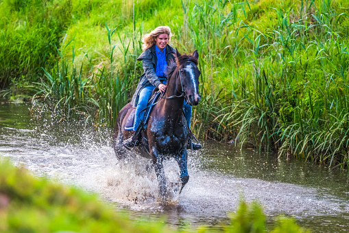 A female, riding her horse on the river