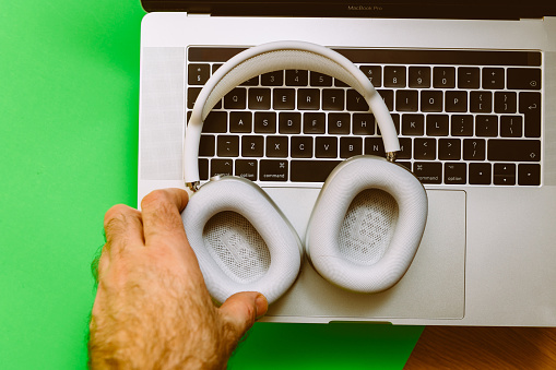 Paris, France - Jan 7, 2020: Man puts new Apple Computers AirPods Max over-ear headphones on the keyboard of M1 MacBook Pro 16 inch laptop