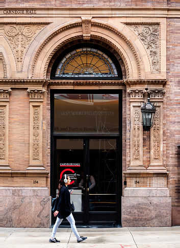 A woman wearing headphones strolls past Carnegie Hall on W 57th Street in Midtown Manhattan.