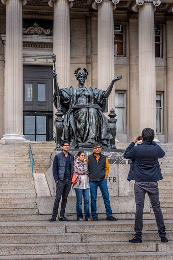 A South Asian family snaps a photo in front of the “Alma Mater” statue  while visiting the campus of Columbia University in the Morningside Heights neighborhood of Manhattan. 

In the background is the Low Library, now used as an administration building and for special exhibits in its rotunda.

The statue’s sculptor was Daniel Chester French (1850-1931,) who, among other famous works, designed the Lincoln statue at the Lincoln Memorial in Washington DC.