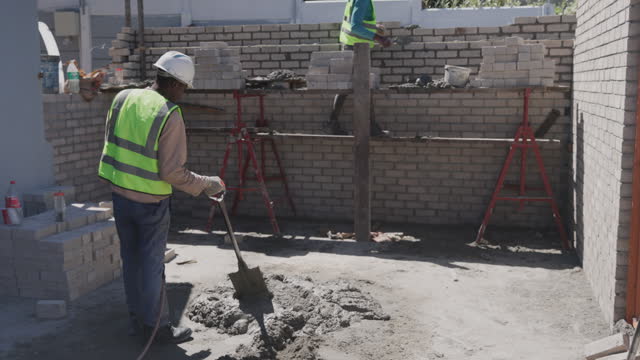Construction, cement and man with shovel at brick wall for housing development, labor and renovation. Bricklayer, builder or contractor at building site with concrete, mix and material for project.