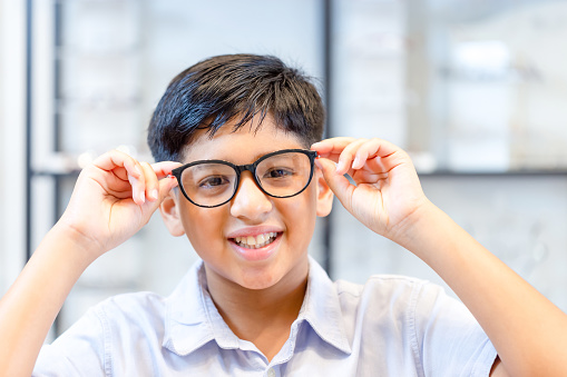 Smiling Indian-thai boy choosing glasses in optics store, Portrait of Mixed race ethnicity kid wearing glasses at the optical store