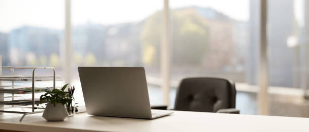 Back view image of a modern minimal bright office with a laptop computer on a white desk.