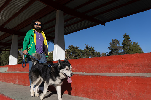 Mexican young man walking with his husky dog in a city park