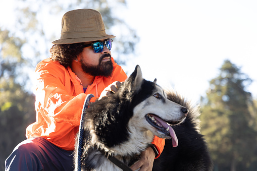 Mexican man with hat and sunglasses, posing in profile with his husky dog