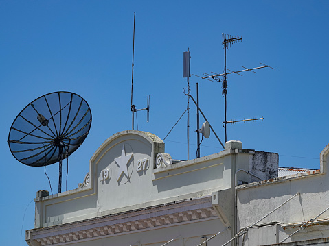 Various aerials and satellite dish on art deco building against blue sky