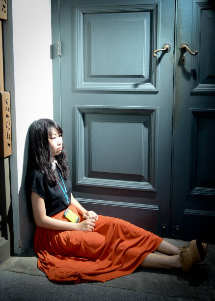 A woman sits on the ground with her hands on her knees. She is wearing a white shirt and shorts