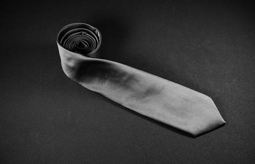 Single plain black necktie rolled on black background close-up view, Single object, No people