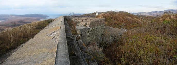 Elevated coastal defense Heavy concrete breastwork and bunker, Fort 9 of Vladivostok fortress fortification buildings overgrown with dry autumn grass, panoramic view