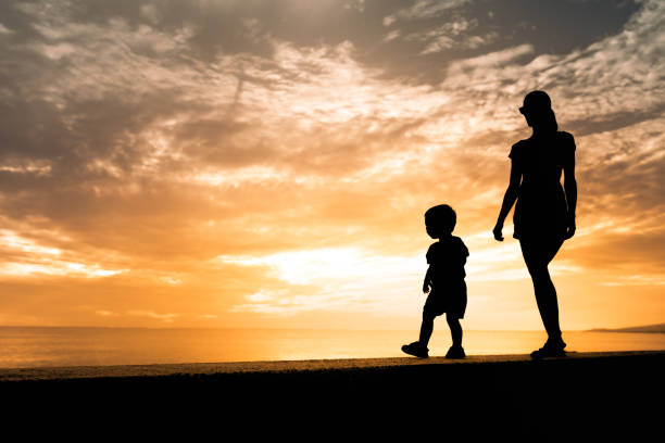 istock Mother and son walking by the ocean at sunset. 1989220452